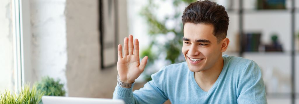 teenage caucasian male waving to a computer screen during virtual interview